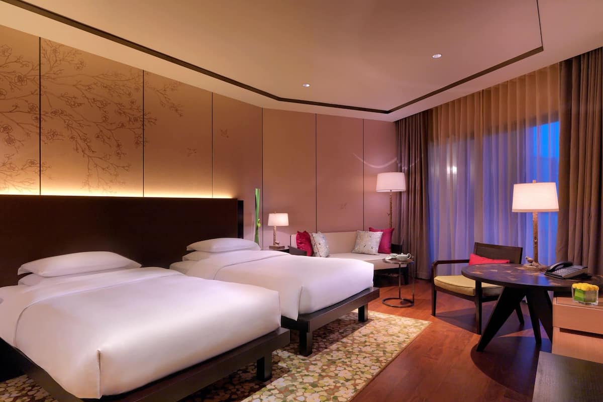 A hotel room with two beds, a desk, a chair, and a view of the night sky.