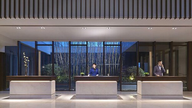 Un'area reception moderna con tre scrivanie, ampie finestre e un soffitto in listelli di legno verticali.