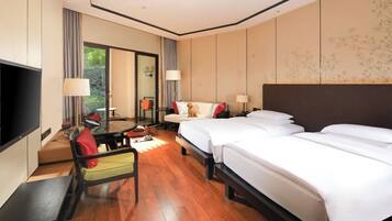 A hotel room with a large bed, a desk, a chair, a TV, and a window with curtains.