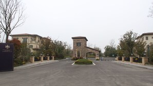 Un ingresso delimitato da cancello con una torre centrale, circondato da alberi ed edifici.