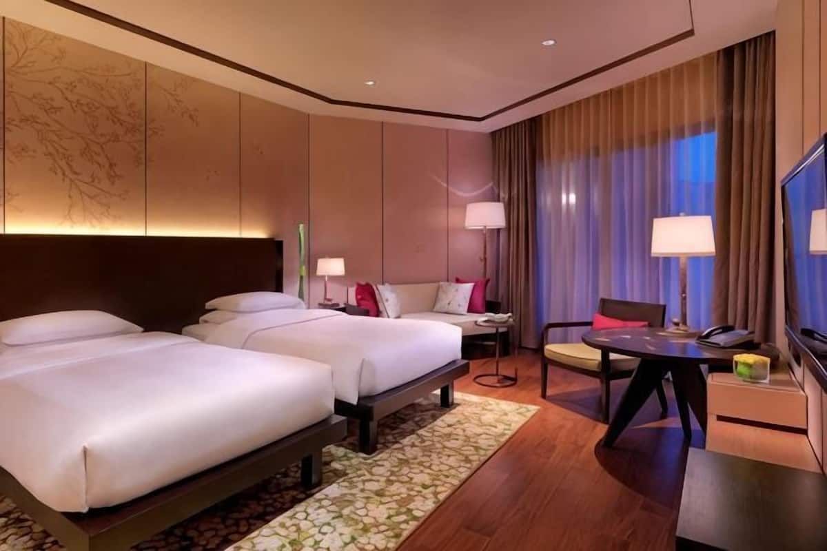 A hotel room with two beds, a desk, a chair, a TV, and a large window with curtains.