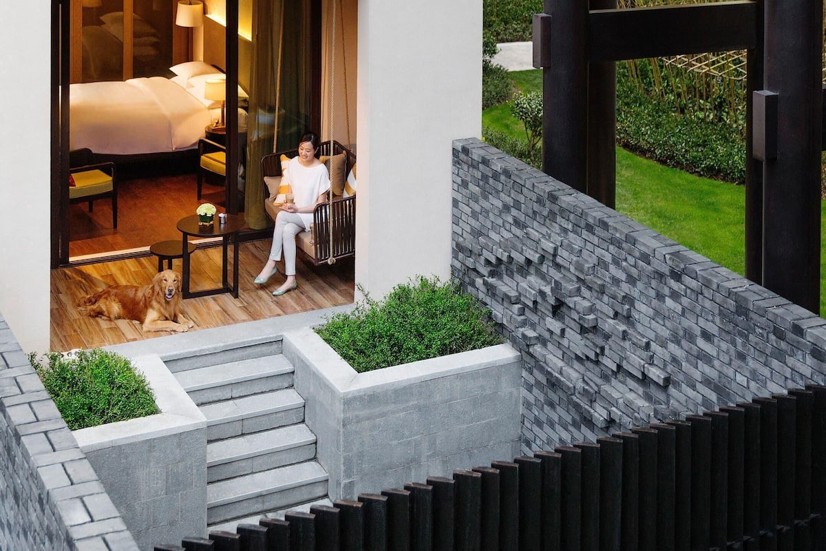 A modern hotel room with a bed, a sitting area, and a view of the garden.