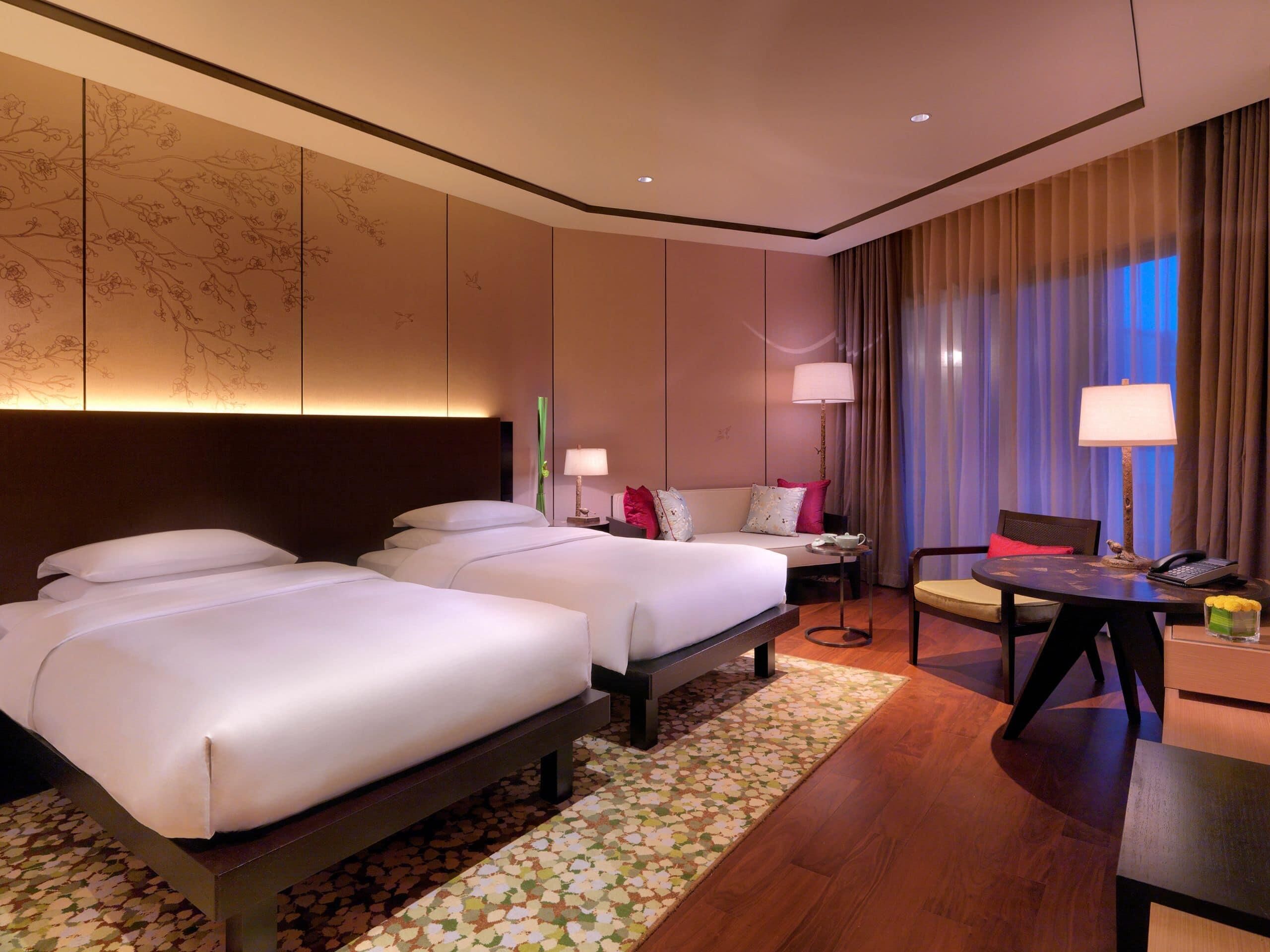 A hotel room with two beds, a desk, a chair, and a view of the night sky.
