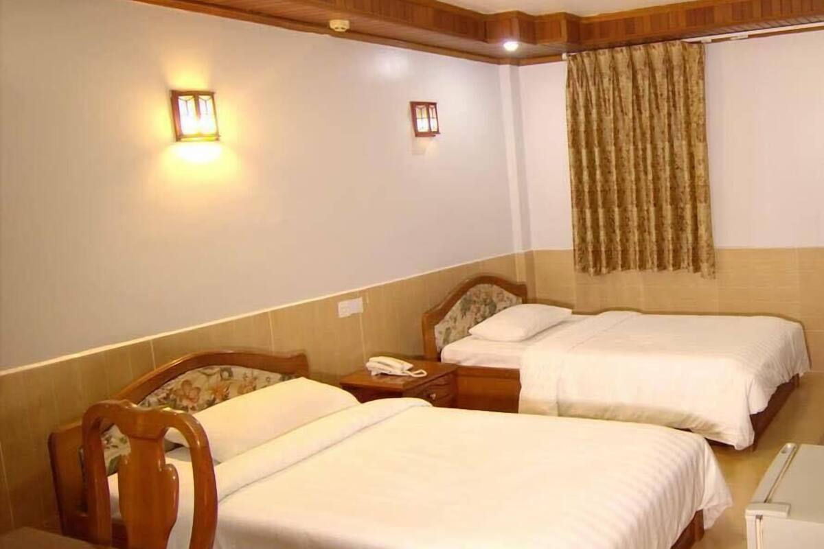 A hotel room with two single beds, a wooden headboard, a bedside table with a lamp, and a curtain on the window.