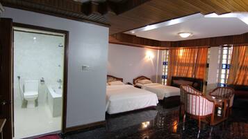 A hotel room with a bathroom, two beds, a sitting area with chairs, and a wooden ceiling.