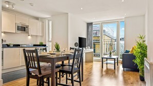 Een modern appartement met keuken, eetgedeelte en woonkamer. Het heeft een groot raam, een flatscreen televisie en een balkon met uitzicht op de stad.