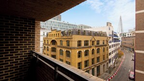 Uitzicht op een stadsstraat vanaf een balkon, met bakstenen gebouwen, een modern glazen gebouw en een hoge spits op de achtergrond.