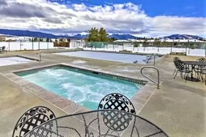 A rectangular pool with a hot tub in the center, surrounded by outdoor seating and a view of mountains.