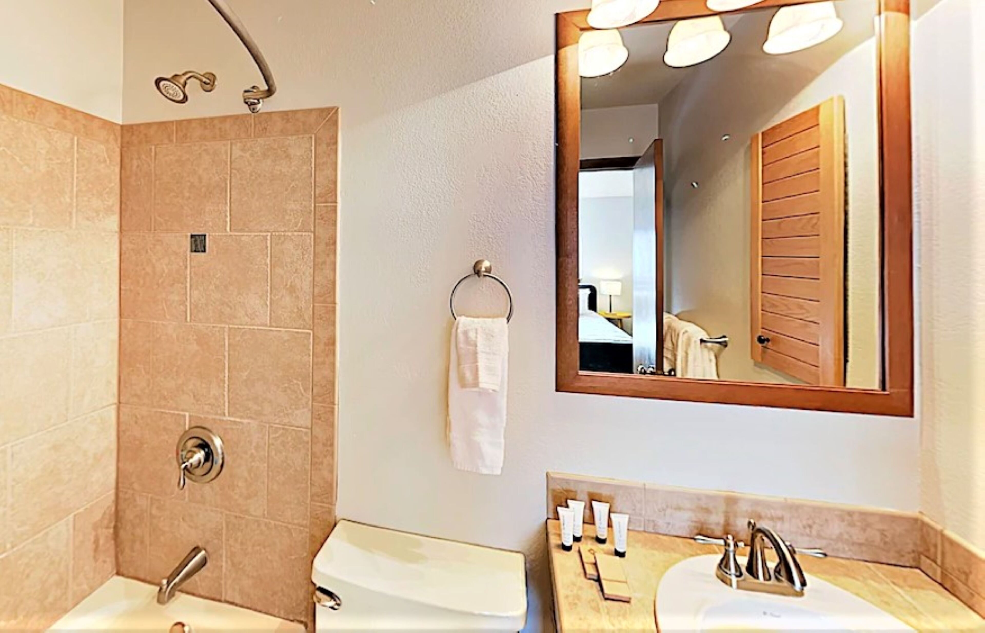 Een badkamer met douche, wastafel, spiegel en toiletartikelen.