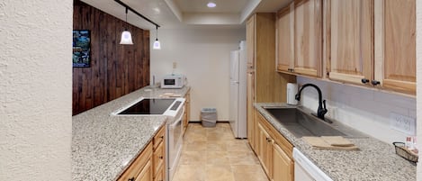 A kitchen with granite countertops, wooden cabinets, a microwave, a refrigerator, and a sink with a black faucet.