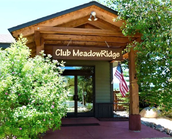 The entrance to Club MeadowRidge with a wooden archway, an American flag, and a well-maintained garden area.