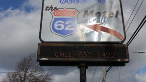Un panneau numérique indiquant le motel Route 62, avec un message de bienvenue et une flèche indiquant la direction.