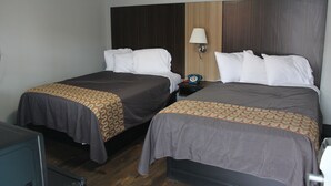 Une chambre d’hôtel avec deux lits, chacun recouvert d’une couvre-lit à motifs, une table de chevet avec une lampe et une tête de lit en bois.