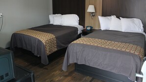 Une chambre d’hôtel avec deux lits, chacun recouvert d’une couvre-lit à motifs, une table de chevet avec une lampe et un téléviseur placé dans un coin.