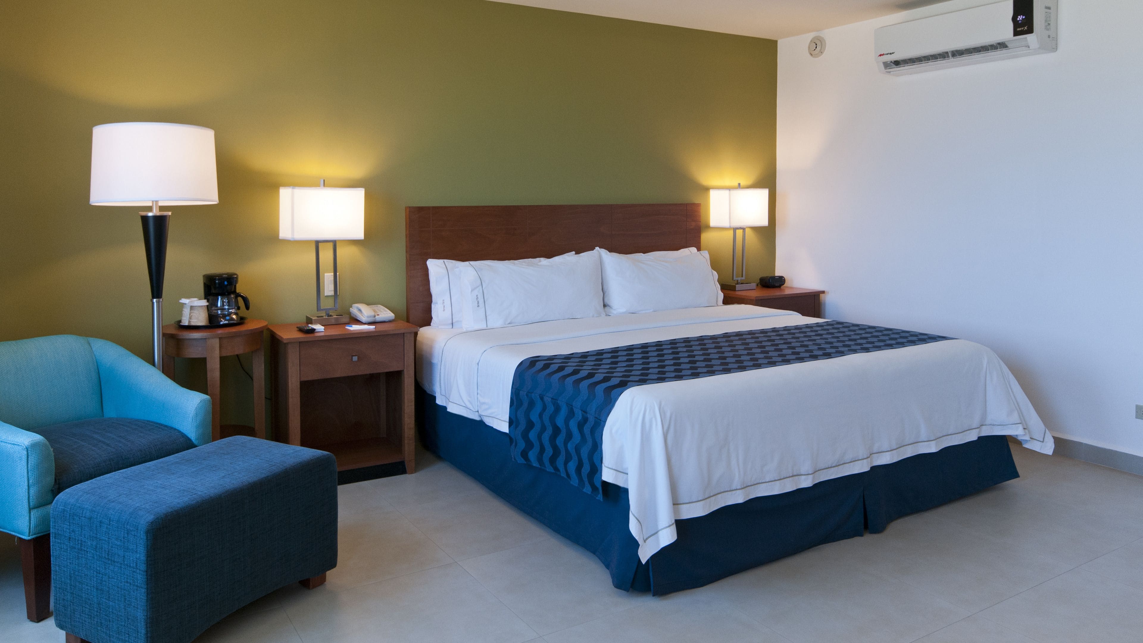 Una habitación de hotel con una cama, dos mesitas de noche, una silla y una lámpara.