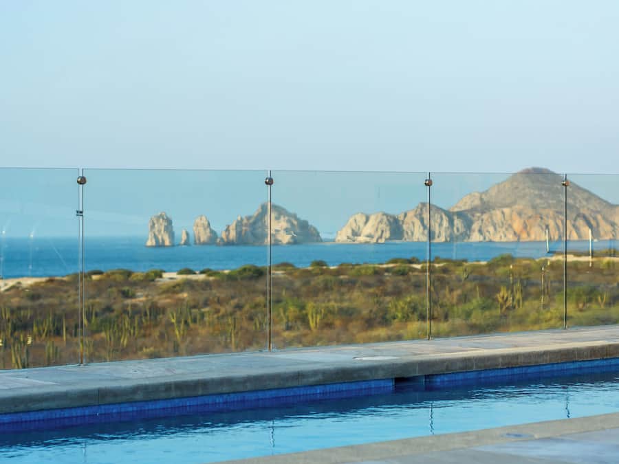 Una piscina con pannelli di vetro trasparente, vista sul mare e formazioni rocciose all'orizzonte.