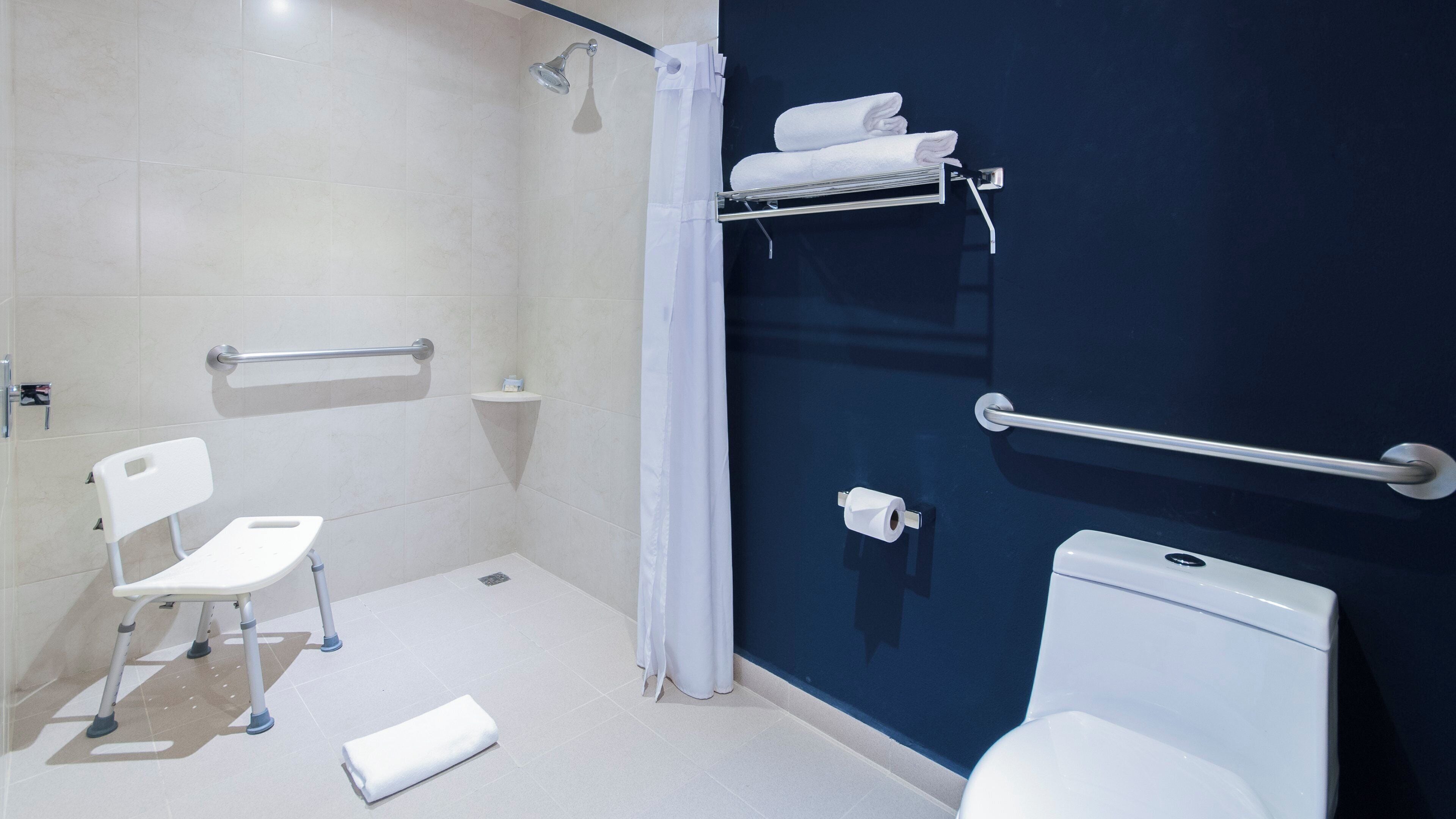 Een badkamer met een douche, toilet en een witte stoel.