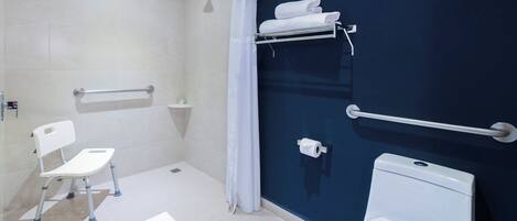 Een badkamer met een douche, toilet en een witte stoel.