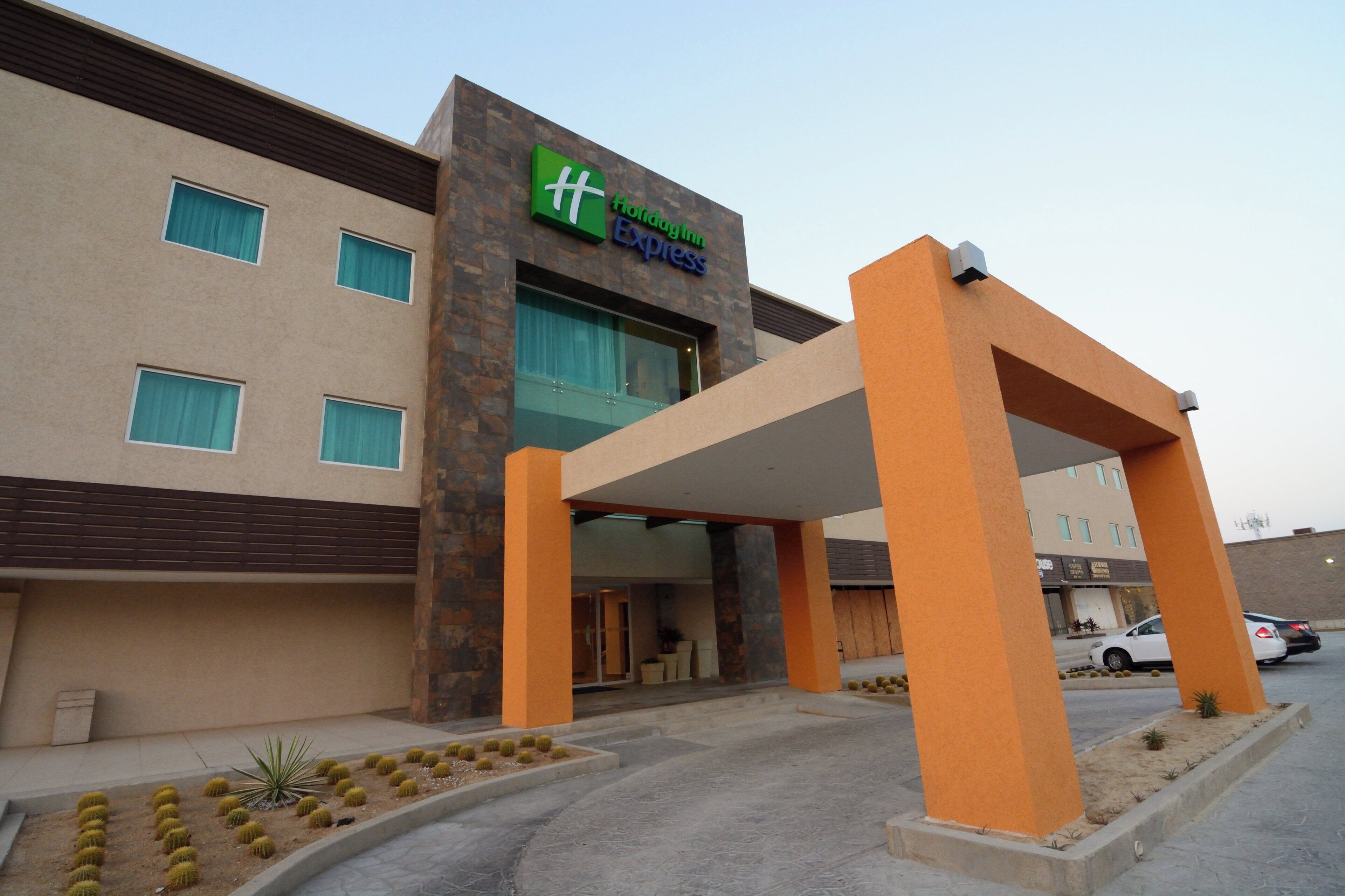 A Holiday Inn Express building with a modern design, featuring a prominent entrance and a parking area with cars.