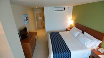 Una habitación de hotel con cama, mesita de noche, lámpara y escritorio con ordenador.