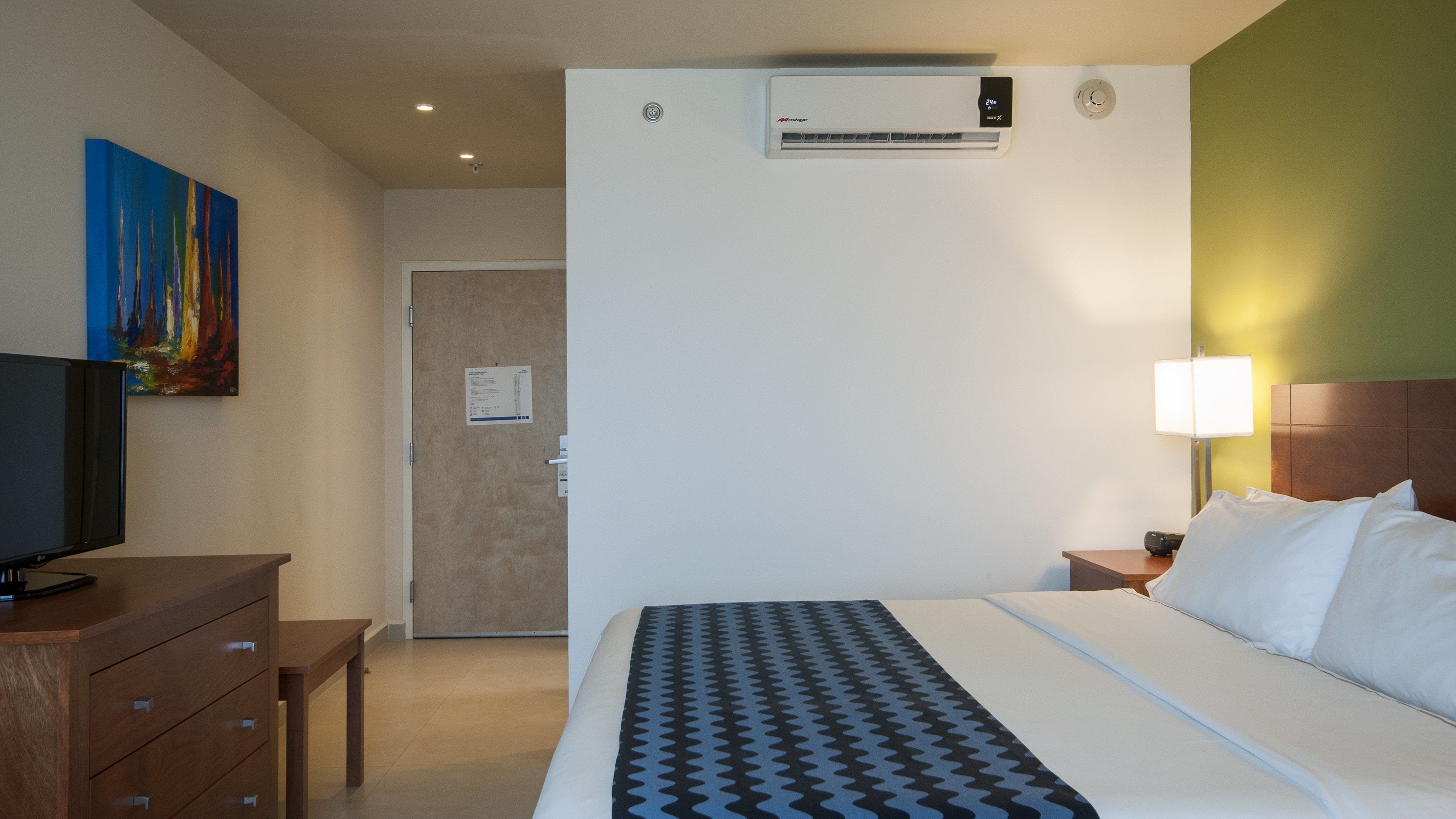 A hotel room with a bed, a TV, a desk, and a painting on the wall.