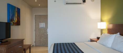 A hotel room with a bed, a TV, a desk, and a painting on the wall.