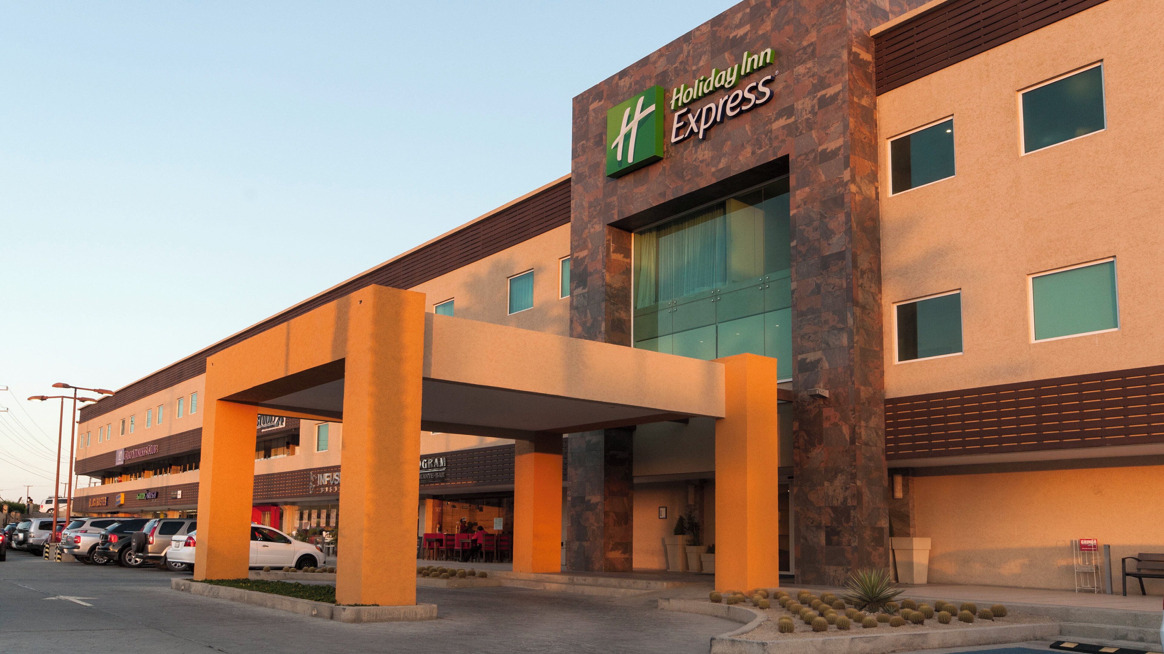 A Holiday Inn Express hotel with a covered entrance, a parking lot, and adjacent businesses.