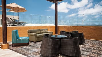 Un área de estar exterior con vista a la piscina, con sillones de descanso y una mesa.