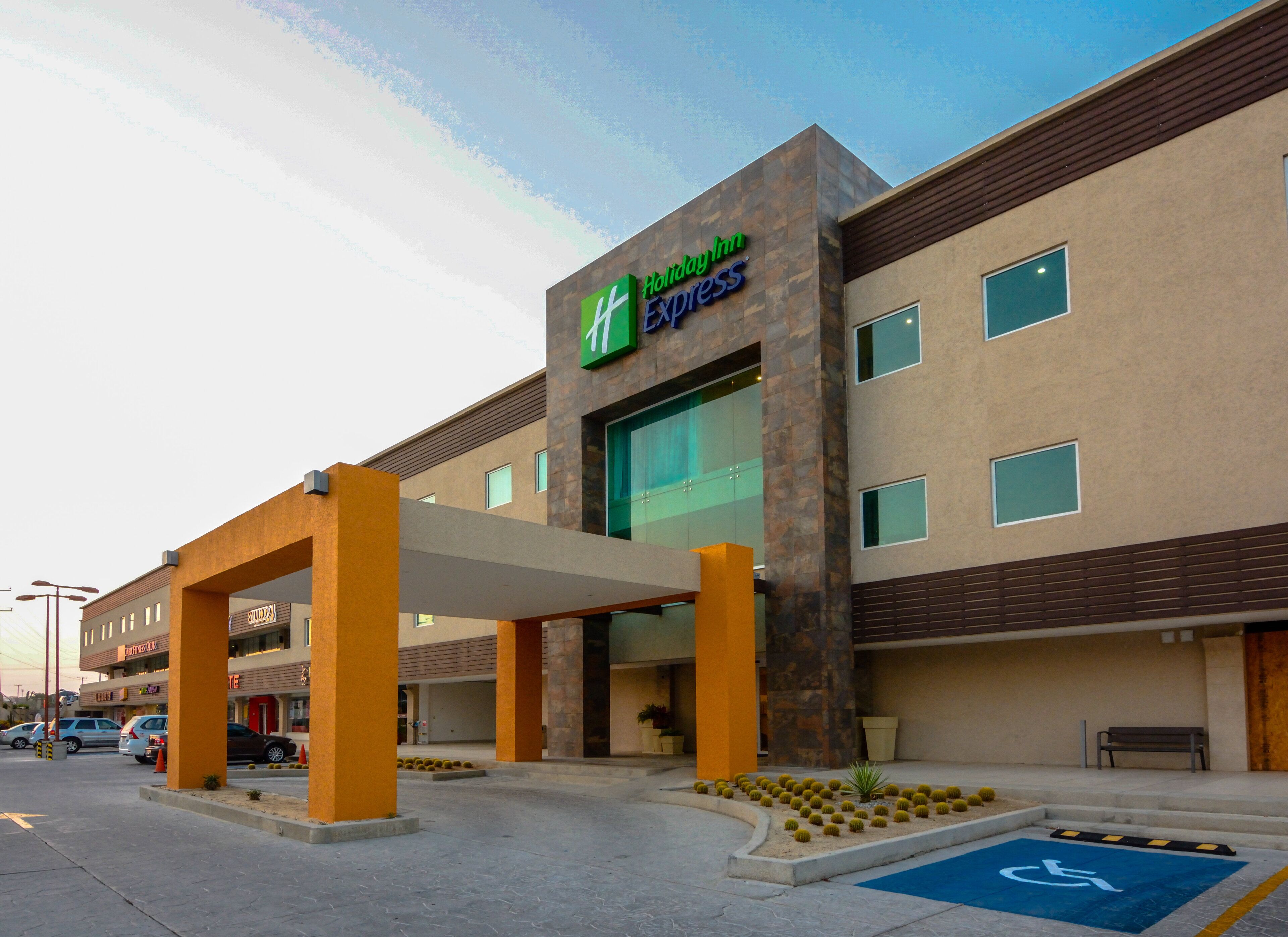 A Holiday Inn Express building with a covered entrance, a handicap parking sign, and a parking lot with several cars.