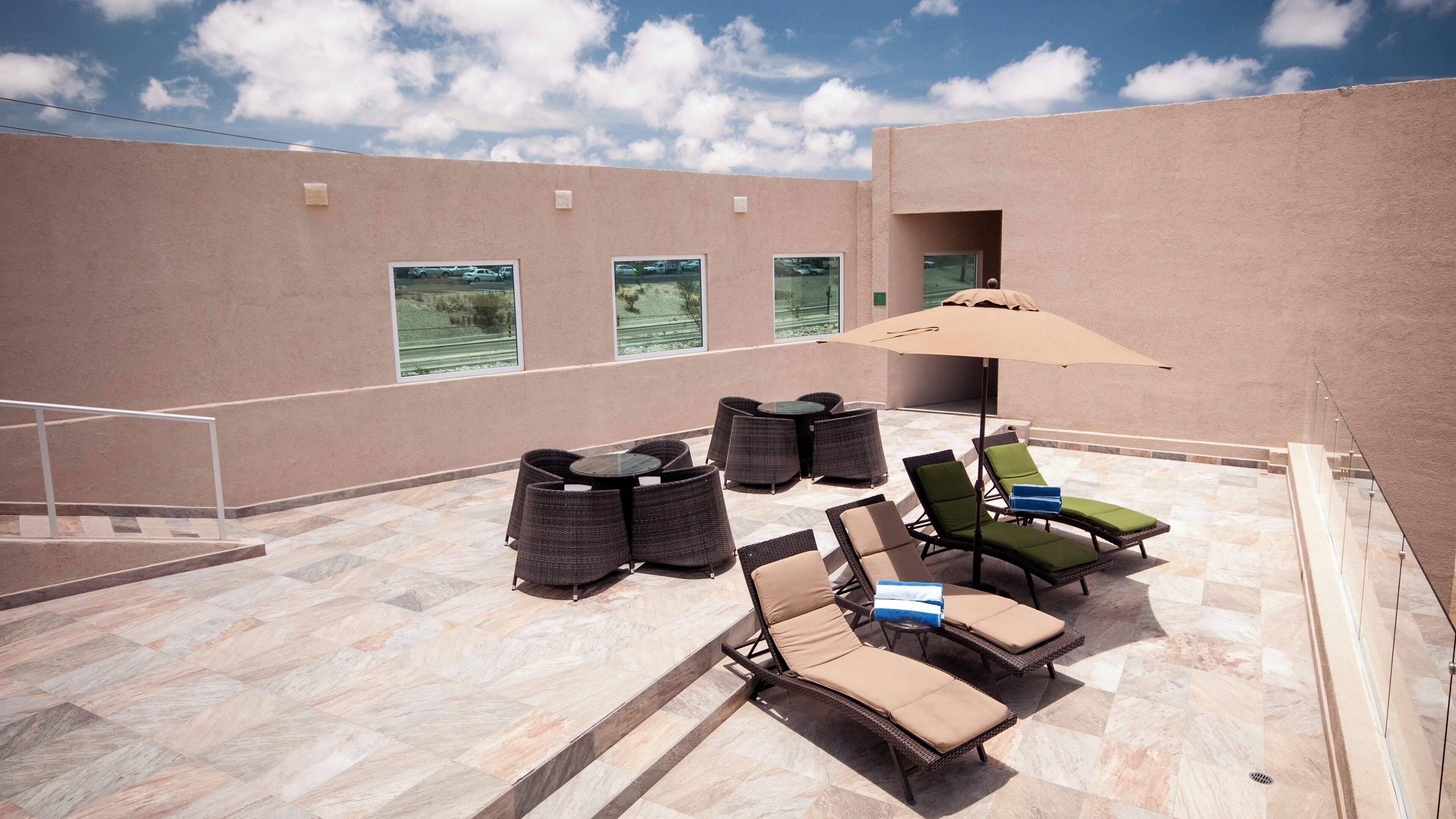 An outdoor patio with wicker furniture, a large umbrella, and a view of the surrounding area.