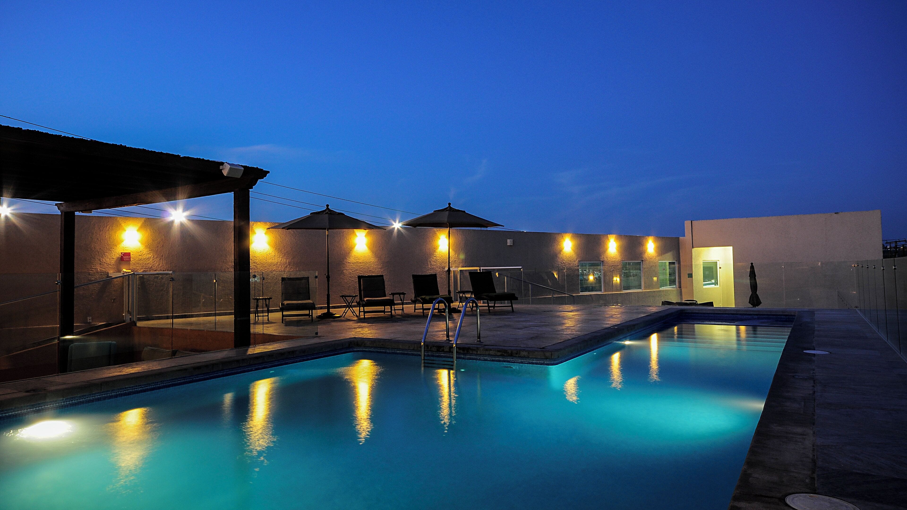 A swimming pool area with lounge chairs and umbrellas, surrounded by walls with exterior lighting.