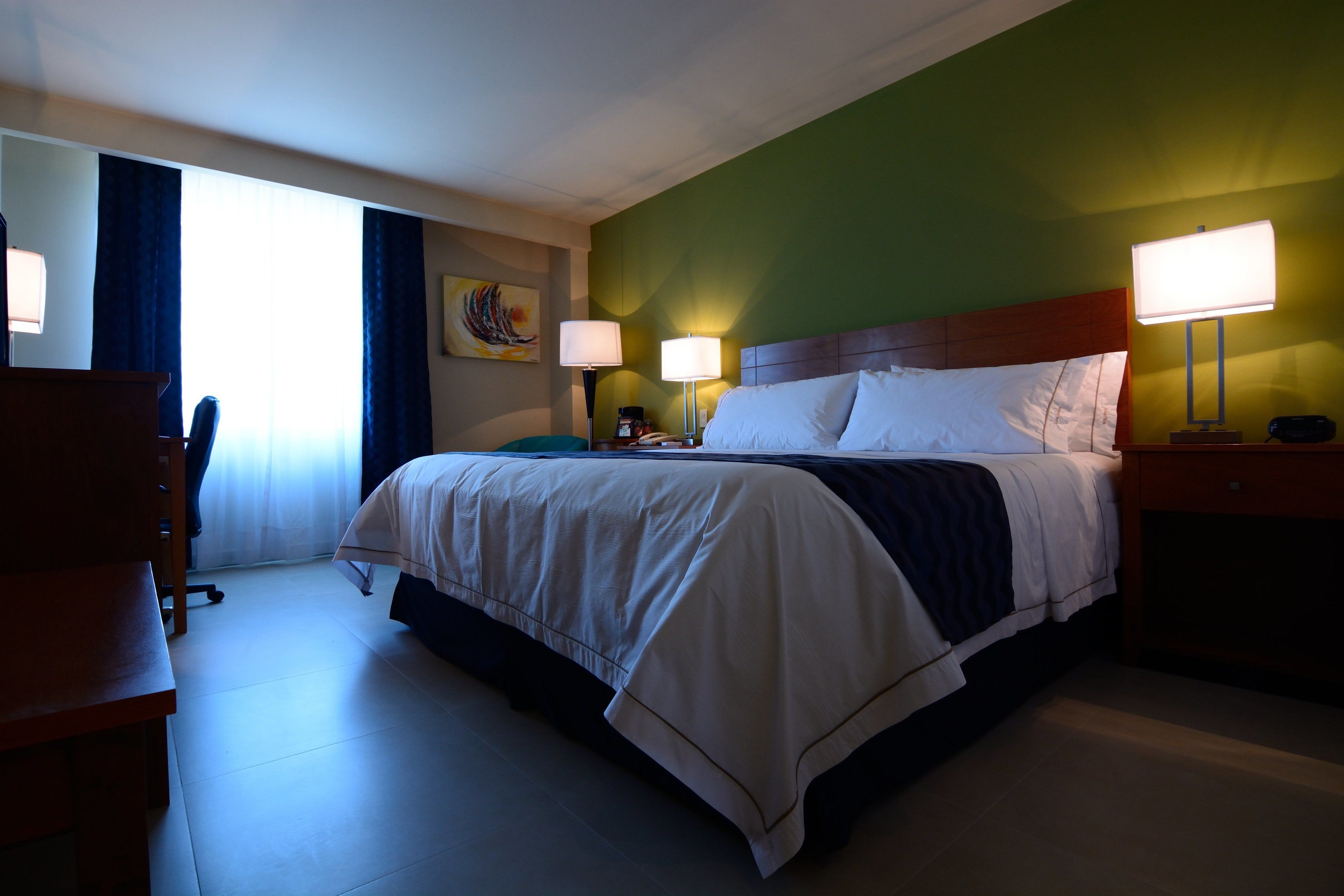 Une chambre d’hôtel avec un grand lit, deux lampes de chevet, un bureau et une chaise.