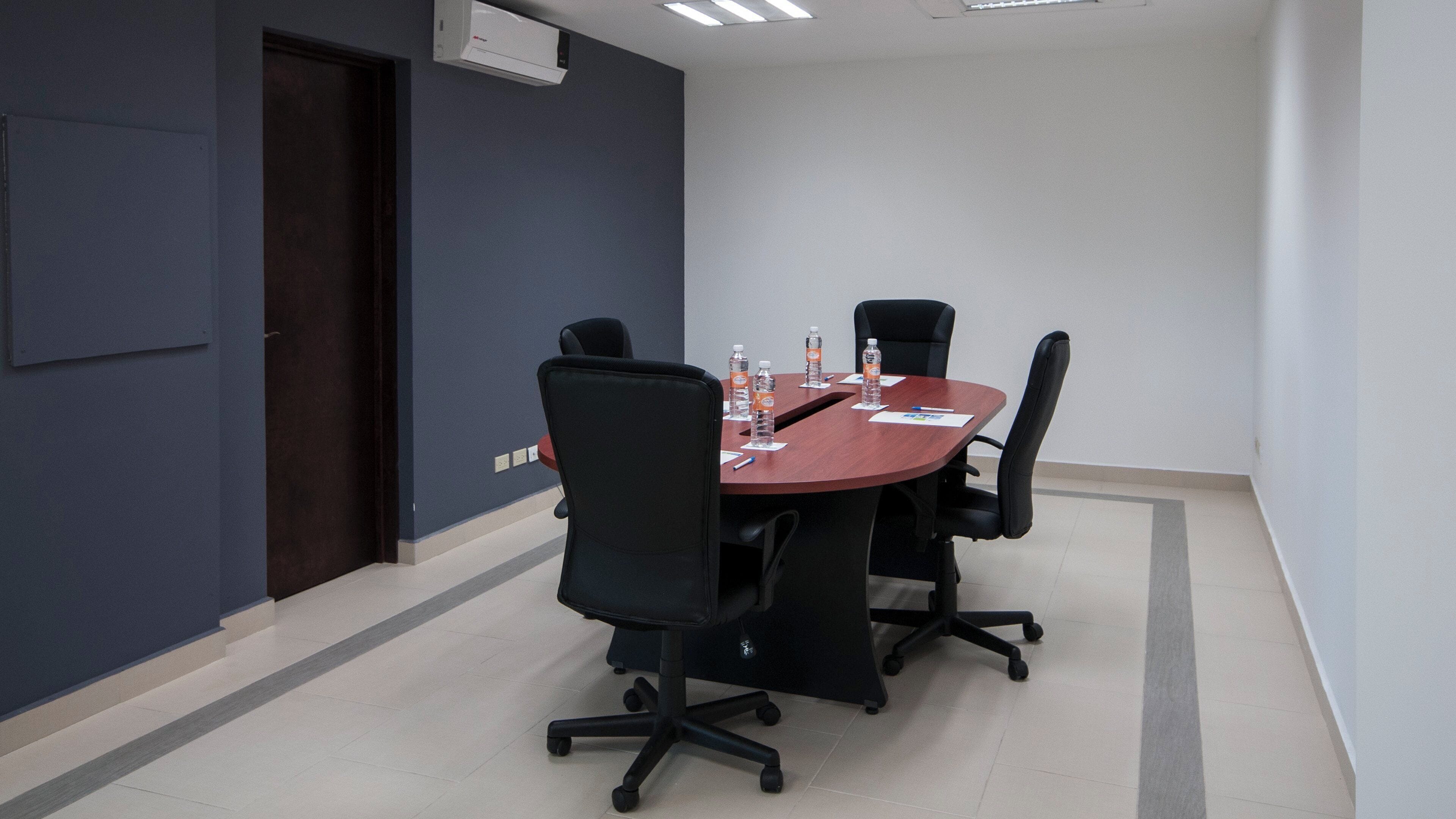 A conference room with a round table, four chairs, and water bottles on the table.