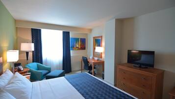 Una camera d'albergo con un letto, una scrivania, una sedia, una televisione e un quadro appeso al muro.