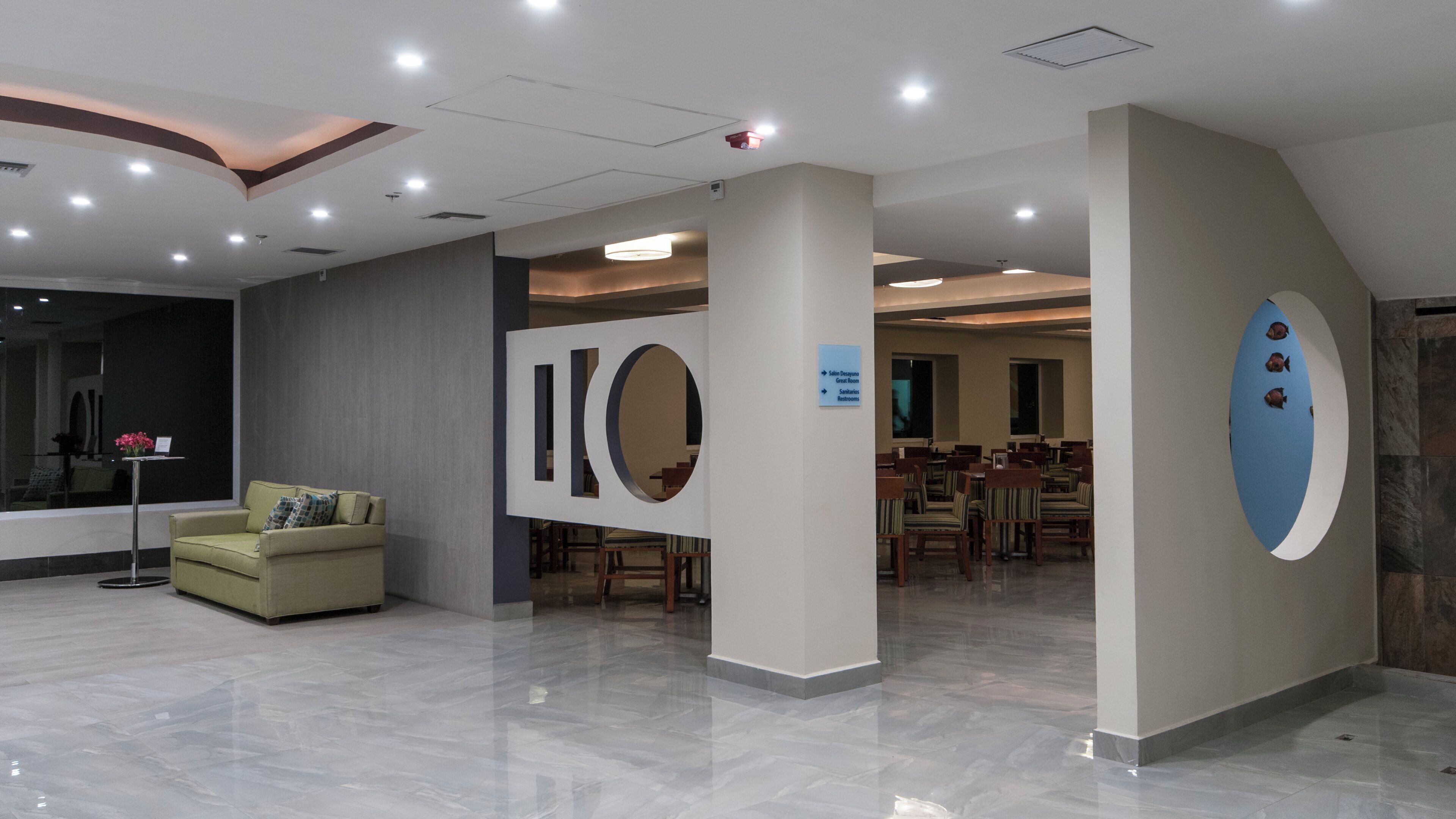 A hotel lobby with a reception desk, seating area, and a sign indicating directions to the Great Room and bathrooms.