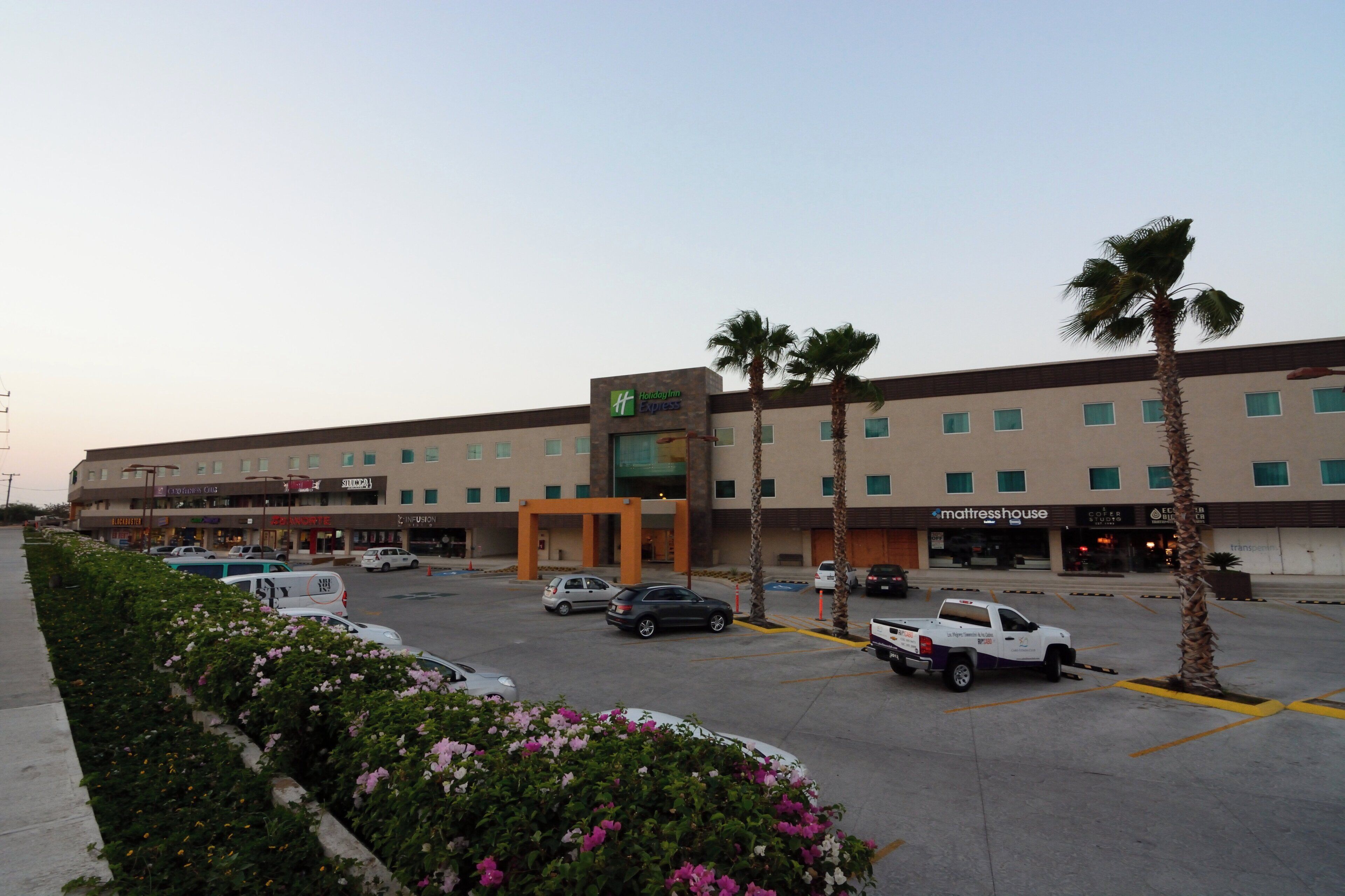 A Holiday Inn Express hotel with a parking lot, palm trees, and various storefronts.