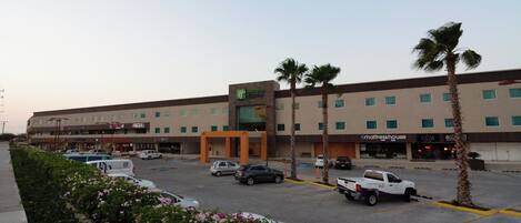 A Holiday Inn Express hotel with a parking lot, palm trees, and various storefronts.