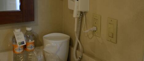 A bathroom with a hairdryer, a mirror, a sink, and toiletries.