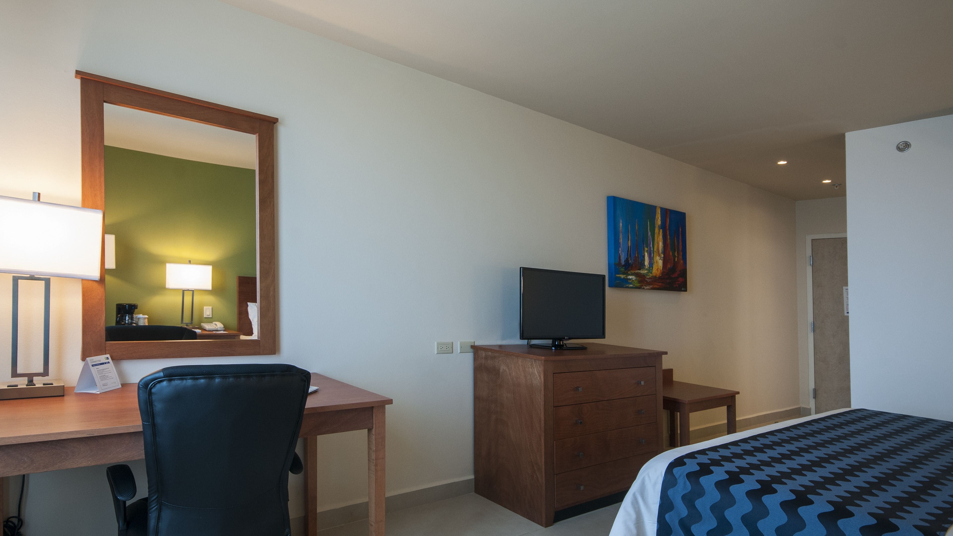 Ein Hotelzimmer mit Schreibtisch, Stuhl, Kommode, Fernseher und Bett.