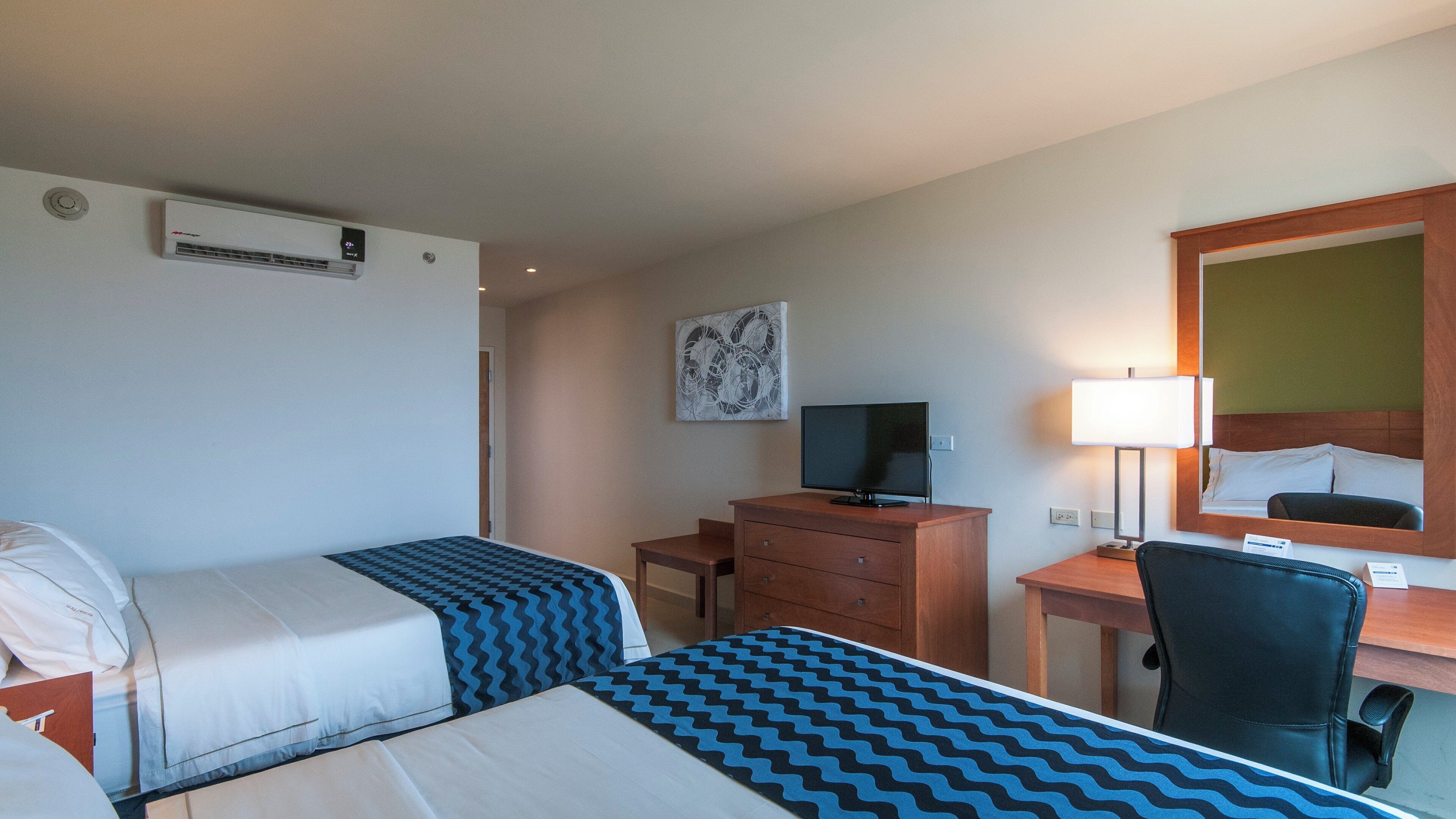 A hotel room with two beds, a desk, a chair, a television, and a mirror.
