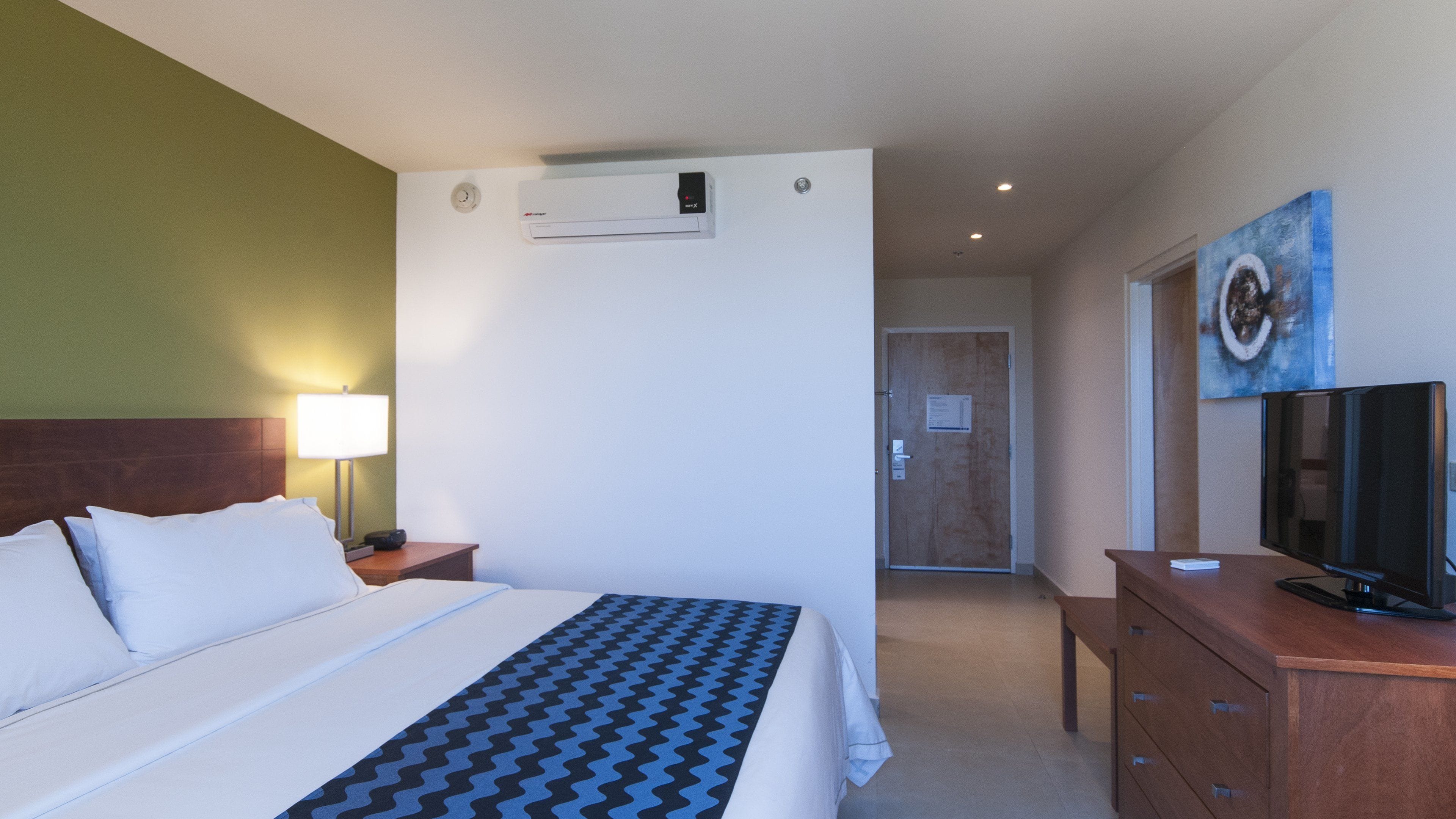 A hotel room with a bed, a desk, a television, and a painting on the wall.