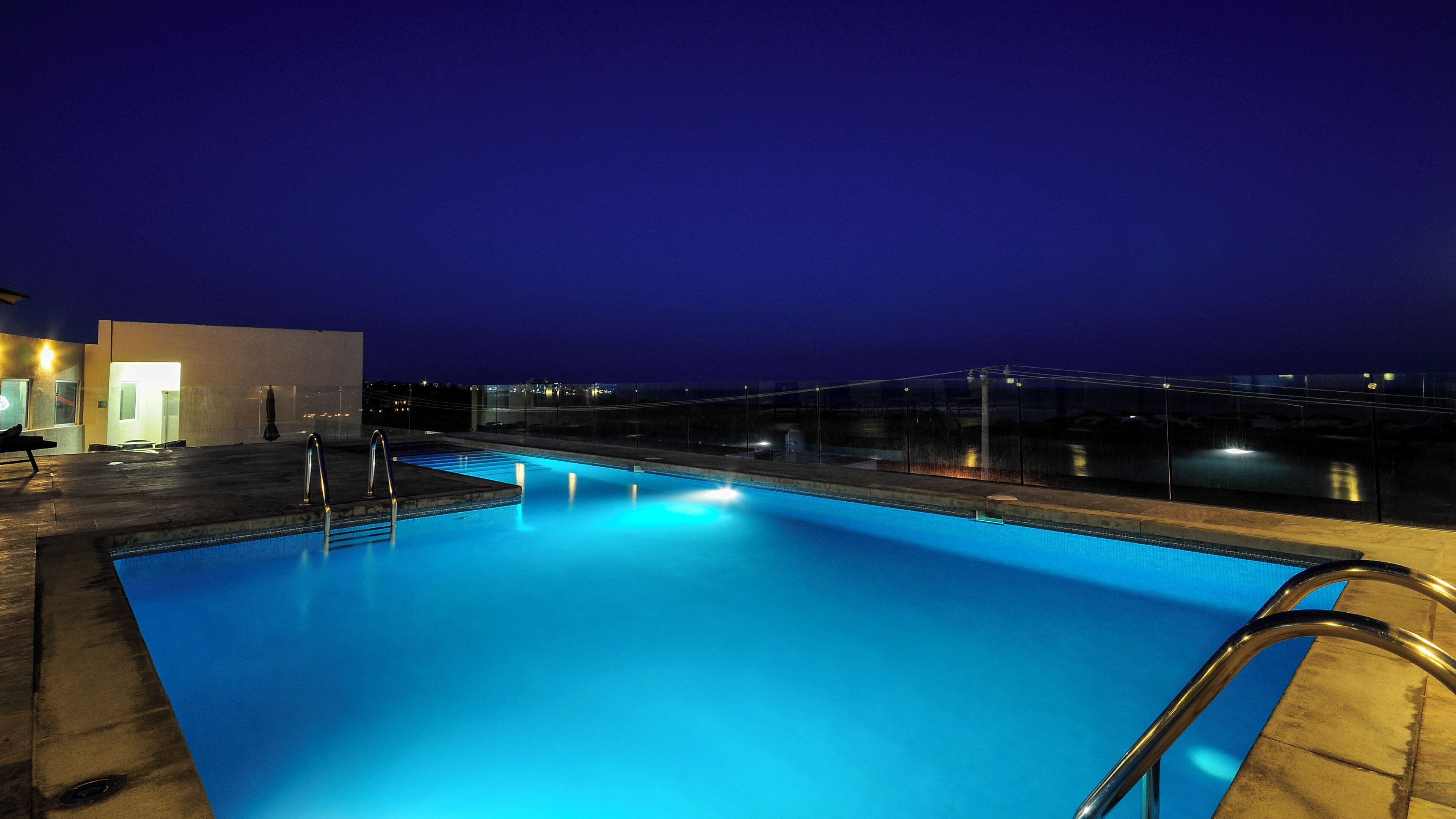 Una piscina con barrera de vidrio y barandillas metálicas, rodeada por un edificio de diseño moderno.