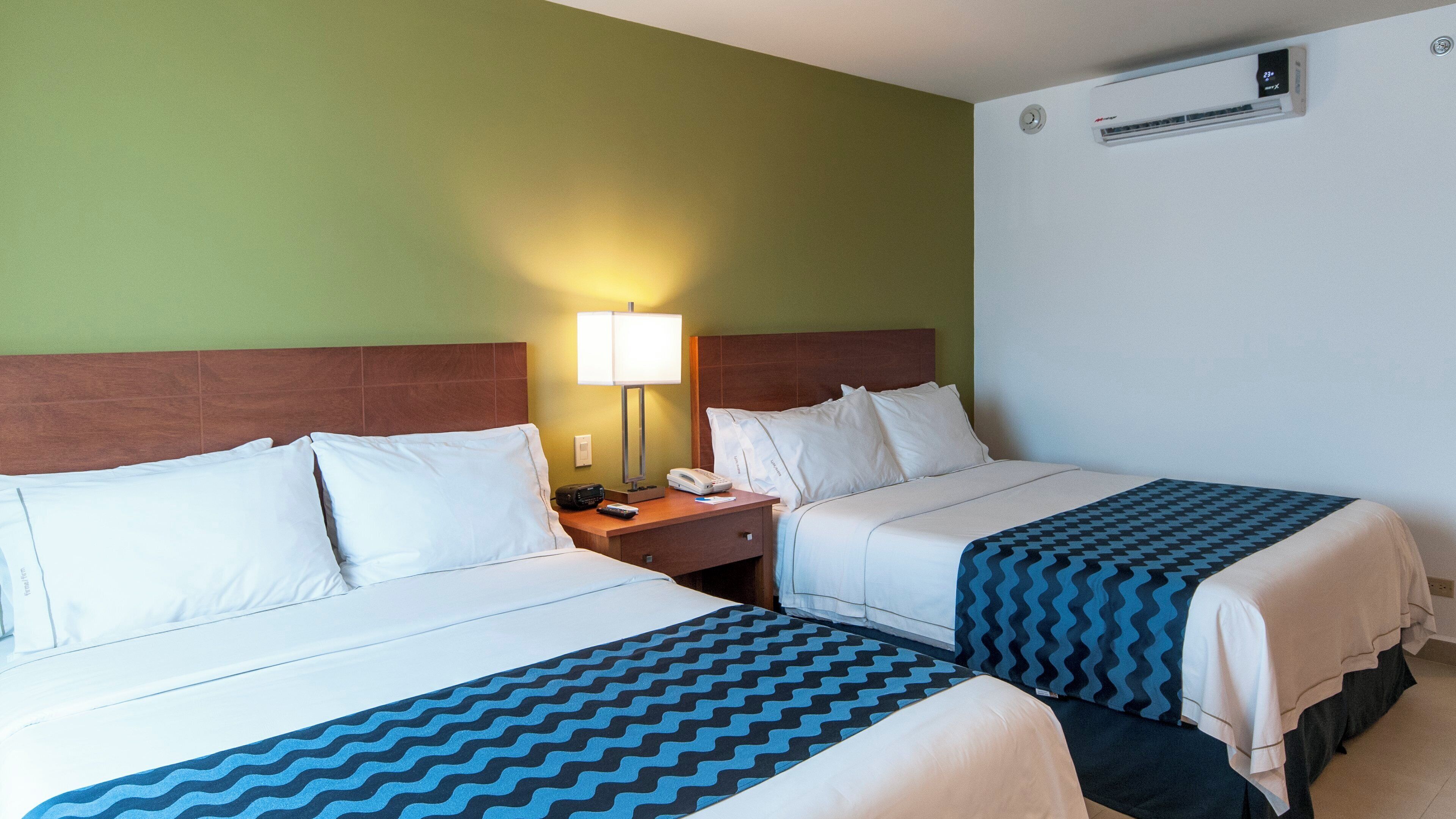 Une chambre d’hôtel avec deux lits, une table de chevet avec une lampe, un téléphone et un appareil de climatisation.