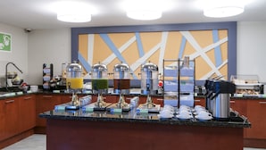 Un comptoir pour le petit-déjeuner équipé de distributeurs de jus, d’une machine à café et d’un présentoir à pain.
