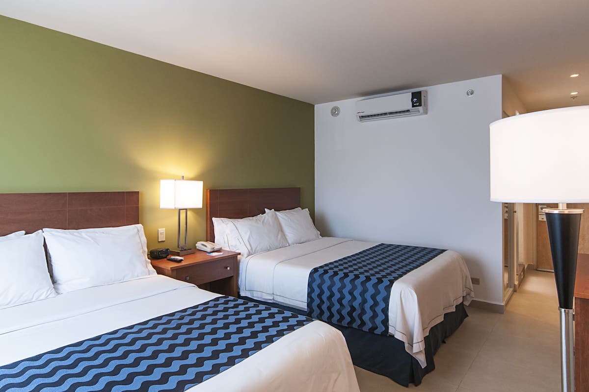 Une chambre d’hôtel avec deux lits, une table de chevet, une lampe, un climatiseur et un bureau avec une lampe.