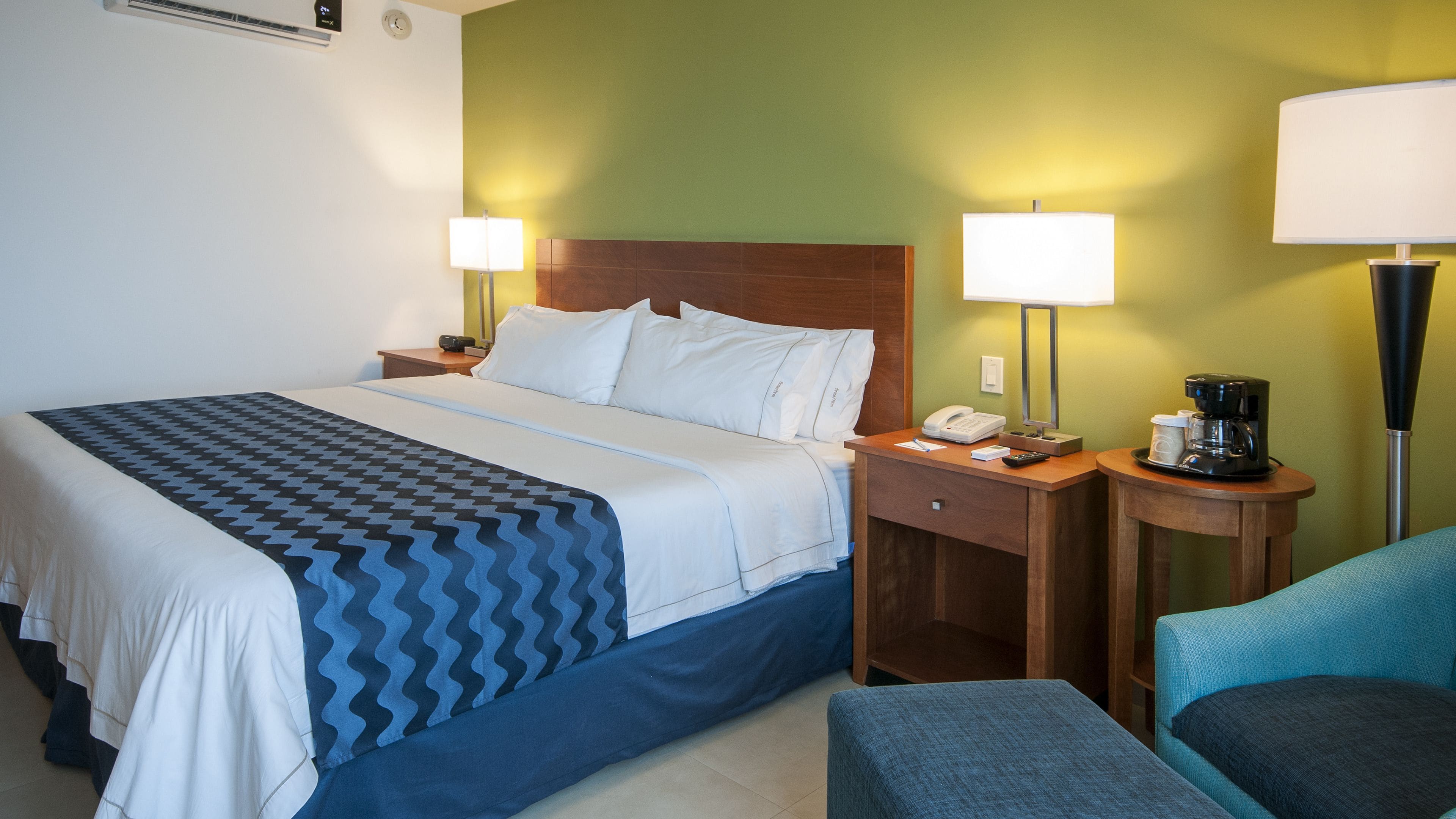 A hotel room with a bed, nightstands, a coffee maker, and a chair.