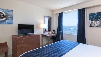 A hotel room with a bed, a desk with a computer, a television, and a window with a view of the city.