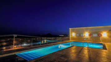 Una piscina con agua cristalina, rodeada por un solárium con baldosas y una pared con carteles informativos.