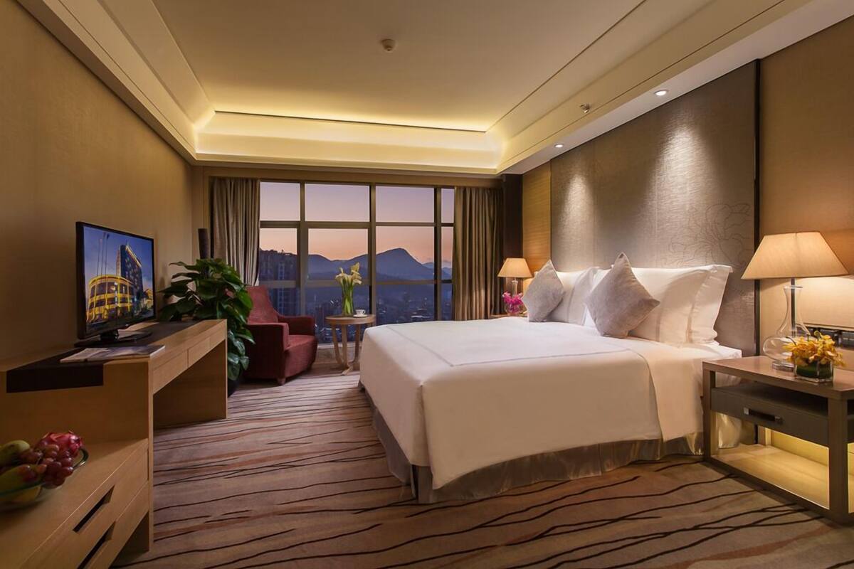 Une chambre d’hôtel avec un grand lit, un bureau avec un ordinateur, une chaise, une télévision et une vue sur les montagnes.