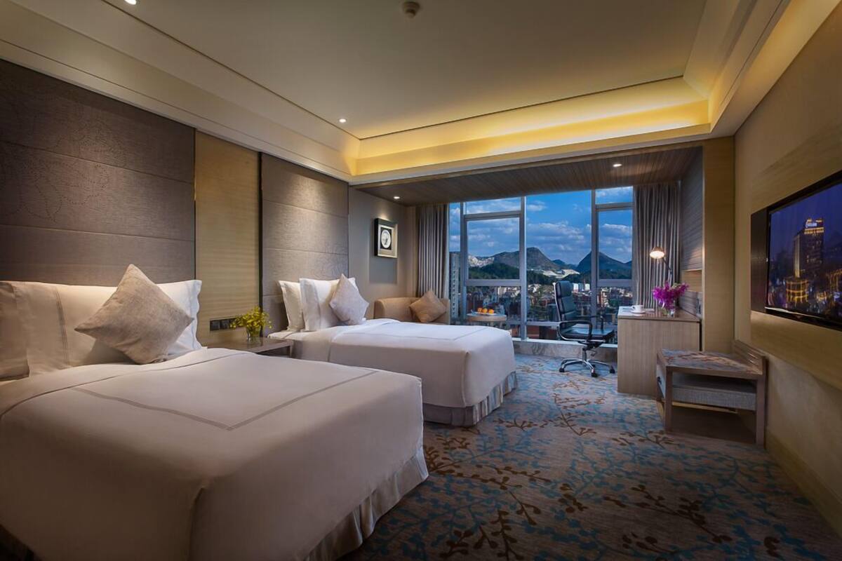 Une chambre d’hôtel avec deux lits, un bureau, une chaise et une grande fenêtre donnant sur la montagne.
